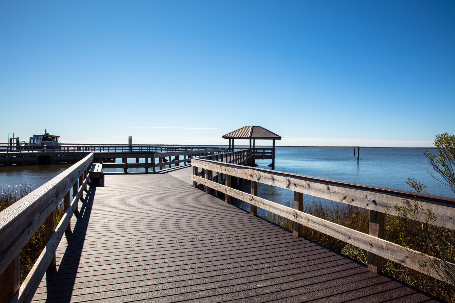 A wooden fishing pier and boardwalk stands over still blue water.